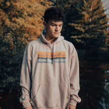 Load image into Gallery viewer, Model wearing sand coloured hooded sweatshirt with horizon design. Forest scenery in the background