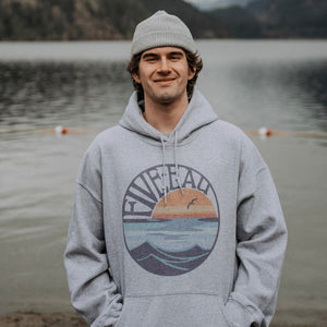 Model wearing grey hooded sweatshirt with Retro Sunset design.  Mountain Lake scenery in the background.