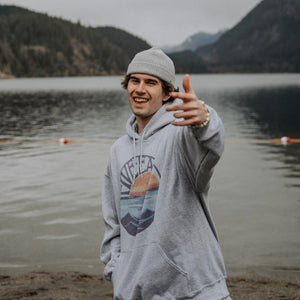 Model wearing grey hooded sweatshirt with Retro Sunset design. Mountain Lake scenery in the background.